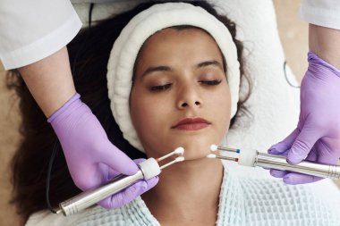 Modern kozmetik prosedürleri uygulayan genç ve mutlu bir kadın. Cilt bakım spa konsepti. Spa Salonu 'ndaki terapistten yüz akımı tedavisi gören güzel bir kadının yakın çekimi..