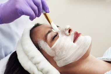 Mükemmel bir güzellik uzmanı, yaşlanma önleyici beyaz bir maskeyi yüzüne bir fırçayla sürer..