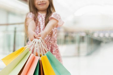 Alışveriş merkezinde alışveriş torbaları tutan mutlu kız. Küçük bir kız elinde çok renkli pastel torbaları kameraya yakın tutuyor. Alışveriş merkezi konsepti, alışveriş merkezi. Reklam için şablon.