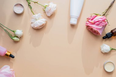 Doğal malzemelerden kozmetik ürünler ve bej arka planda çiçek ve güller. Krem, losyon, beyaz tüplere jöle..