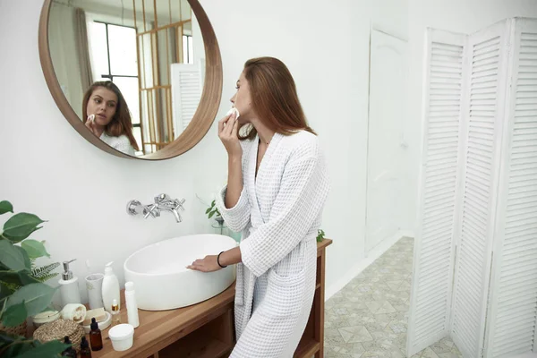 Una guapa morena limpia su piel con una almohadilla de algodón con agua micelar o un limpiador —  Fotos de Stock