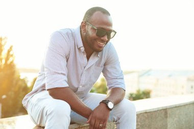 Güneş gözlüklü koyu tenli bir adam parkta oturuyor. 20 'li yaşların sonlarında bir yaz günü filtrelenmiş bir şekilde parkta oturan siyahi bir adamın portresi..