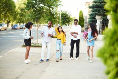 Farklı milletlerden genç ve güzel insanlar şehirde dolanıp konuşuyorlar. Gülümseyen Genç Dostlar Dışarıda Birlikte Yürüyorlar.