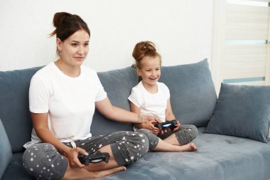 Anne ve kızı bilgisayar oyunu oynuyorlar. Küçük bir kız oyun konsolu oynuyor..