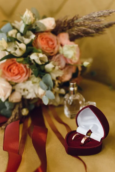Wedding bridal bouquet of roses and eucalyptus branches next to a box of wedding rings on yellow velvet. Wedding and love concept.