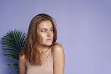 Mor arka planda tropikal palmiye yaprağıyla güzel bir esmerin portresi. Güzellik, cilt bakımı ve yaz tatili konsepti.