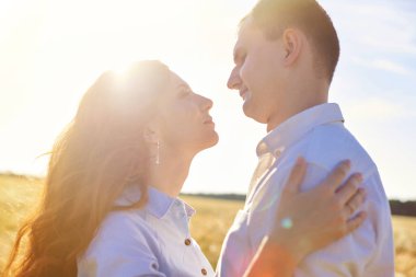 Gülümseyen mutlu çift. Beyaz tişörtlü yakışıklı beyaz adam sarı saçlı, gülümseyen bir kıza nazikçe sarılıyor.