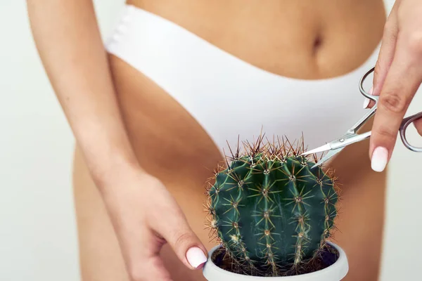 La niña corta un cactus grande con tijeras en el área de la ingle. El concepto de higiene íntima, depilación y depilación, afeitado profundo del bikini — Foto de Stock