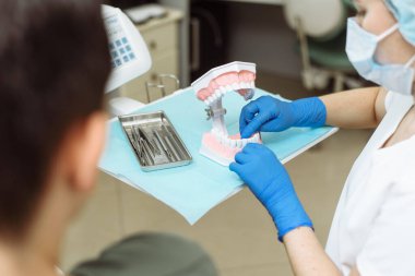 Hasta dişlerini nasıl düzgün fırçalayacağına bakıyor. Diş hekimi yapay çene üzerinde dişlerinizi diş ipiyle nasıl fırçalayacağınızı açıkça gösteriyor.