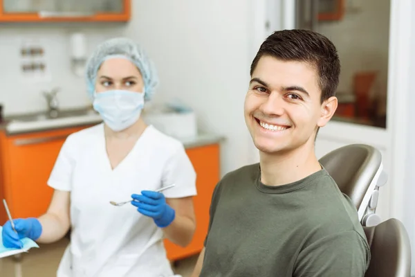 Spokojenej Pacient Zubařském Křesle Mladým Mužem Stojí Ošetřující Lékař — Stock fotografie