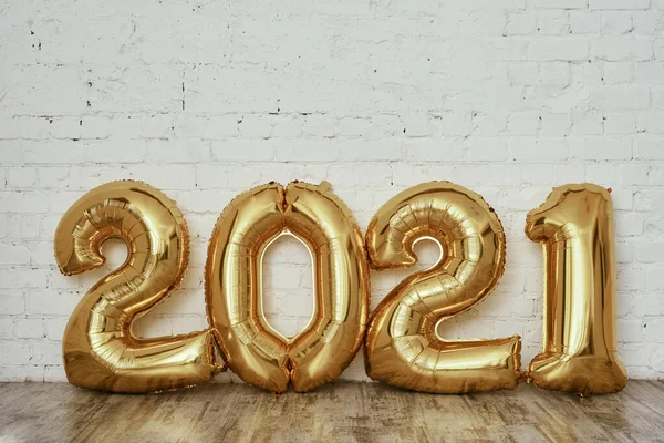 Gold foil balloons in the form of numbers 2021 on white brick wall. New year 2021 celebration. Flat lay.