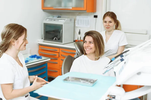 歯科診療所で治療の準備をしている患者さんの女の子と話す医療歯科チーム。女性歯科医と彼女のアシスタントで歯医者と話す女性患者 — ストック写真