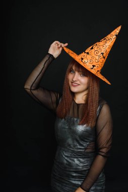 Siyah arka planda turuncu şapkalı ve cadı kostümlü gülümseyen genç kadın. Boşluğu kopyala