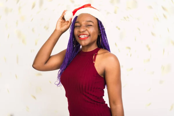 Szexi új év fekete nő csinos arc piros ruhában, fényes töltsük fel piros karácsonyi Mikulás kalap mosoly, pózol fehér háttér konfetti — Stock Fotó