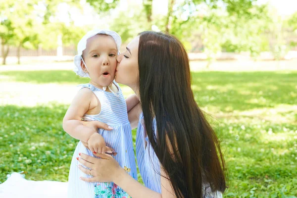 Uma mãe está a beijar uma menina surpresa. Mãe e filha está ao ar livre — Fotografia de Stock