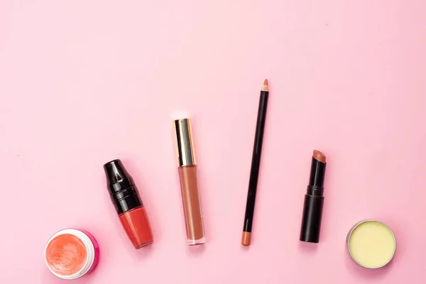 Lip balm, lipstick, gloss and pencil for lip contour on a pink background. Various lip products