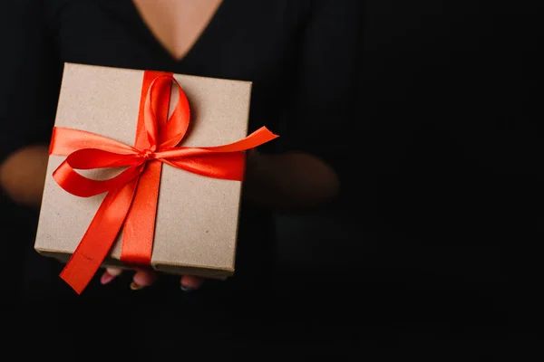 Een zwarte vrouw houdt een kerstcadeau vast met een rood lint in haar handen. Cadeauconcept voor het nieuwe jaar. Kopieerruimte — Stockfoto