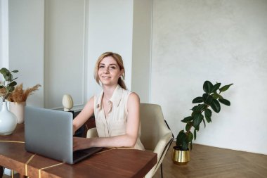 Bilgisayarla çalışan çekici genç bir kadın kameraya bakıp gülümsüyor.