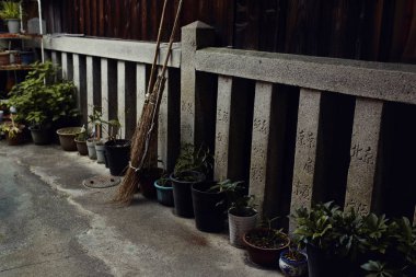 Geleneksel Japon Kyoto, Japonya için bir mahallede detaylar dizayn. Rustik süpürge ve Saksı bitkileri sit karşı eski bir beton çit dağınık.