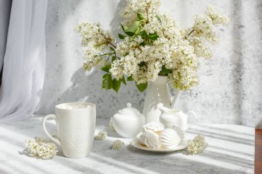 Bir buket beyaz leylak, bir fincan marşmelovlu kahve, bir tabak krema, bir şeker kasesi ve süt sürahisi, eski bir kitap. Kartpostal. Günaydın..