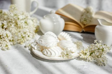 Bir buket beyaz leylak, bir fincan marşmelovlu kahve, bir tabak krema, bir şeker kasesi ve süt sürahisi, eski bir kitap. Kartpostal. Günaydın..