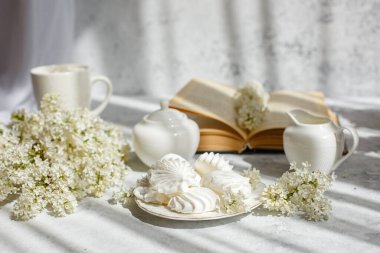 Bir buket beyaz leylak, bir fincan marşmelovlu kahve, bir tabak krema, bir şeker kasesi ve süt sürahisi, eski bir kitap. Kartpostal. Günaydın..