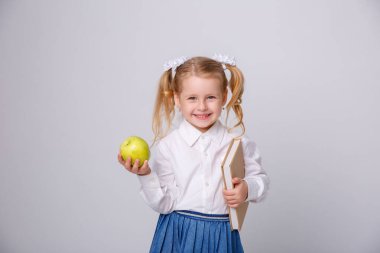 Okul üniformalı küçük bir kız beyaz bir arkaplanda kitap okuyor.