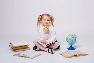 Okul üniformalı küçük bir kız beyaz bir arkaplanda kitap okuyor.