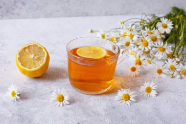 Papatya çiçekli bir fincan çay ve beyaz arka planda limon.