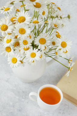 Bir fincan papatya çayı ve vazoda bir buket papatya.