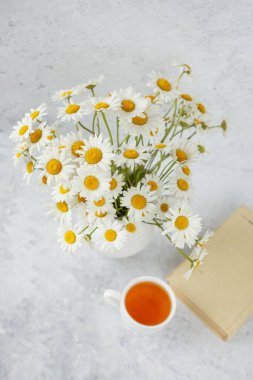 Bir fincan papatya çayı ve vazoda bir buket papatya.