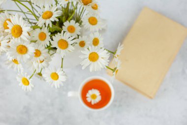 Bir fincan papatya çayı ve vazoda bir buket papatya.