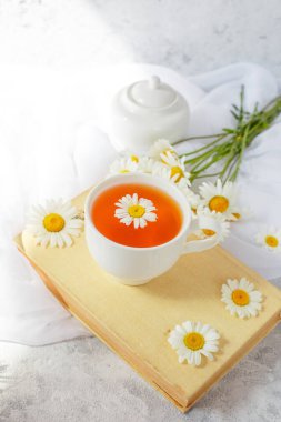 Hayat dolu bir vazo, papatyalar bir fincan çay ve arka planda eski bir kitap.