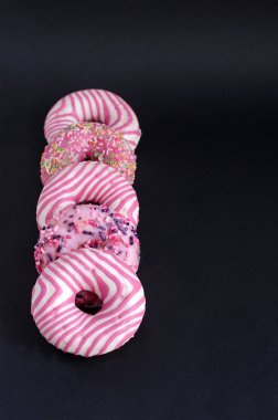 Siyah arka planda pembe kremalı çörekler yan yana uzanıyorlar. Dikey arkaplan, seçici odak.