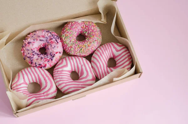 Donuts with pink icing lie in an open box on a pink background. Horizontal background, selective focus.