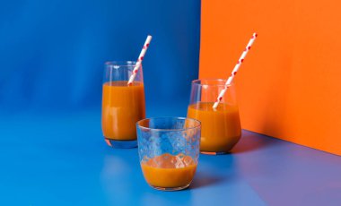 Cam bardakta balkabağı suyu ve 3 boyutlu mavi ve turuncu renkli pipetler, kopyalama alanı olan sonbahar doğal sağlıklı içecek konsepti.