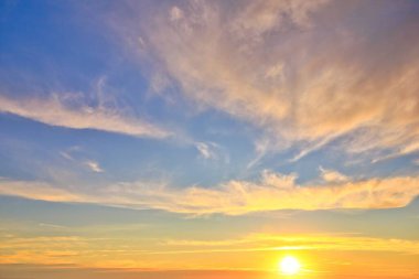 Yeni Zelanda gökyüzü ufuk çizgisine batan parlak bir güneşin yerini alıyor ve bulutları ılık sarı renklerle aydınlatıyor..