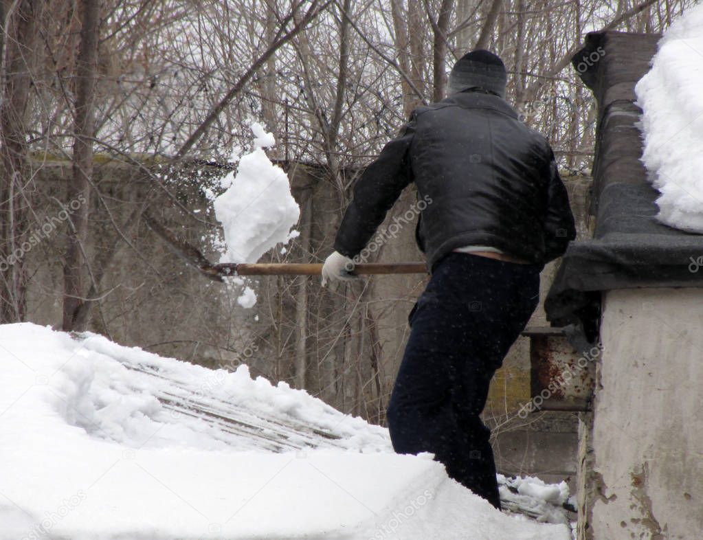 A man removes heavy snow from the roof of a house. Dangerous weight on roof.