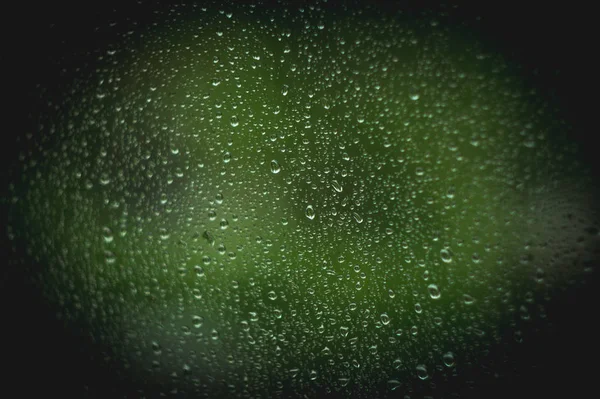 Hujan tetes abstrak pada kaca jendela dengan latar belakang pohon hijau kabur — Stok Foto