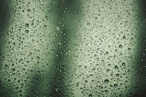 Абстрактні краплі дощу на віконному склі з розмитим зеленим фоном дерева — стокове фото