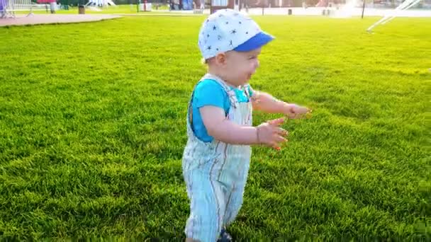 Ребенок неуклюже ходит по ярко-зеленой лужайке и падает — стоковое видео