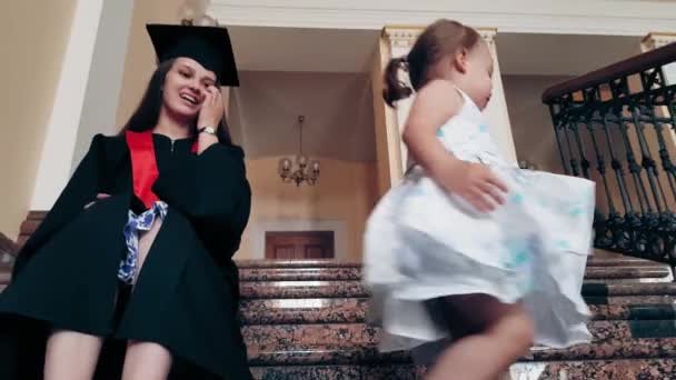 Chica graduada con su hijo en el pasillo de la universidad — Vídeo de stock