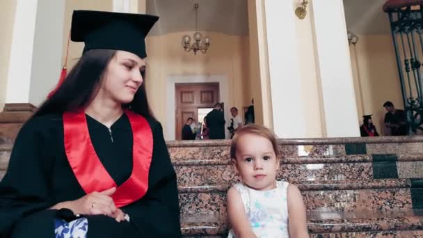 Chica graduada con su hijo en el pasillo de la universidad — Vídeos de Stock