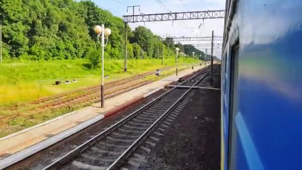 Pociąg pasażerski przechodzi przez małą stację kolejową bez zatrzymywania się. Widok z okna samochodu, autobusu, pociągu. Podróż z pociągu w słoneczny dzień — Wideo stockowe