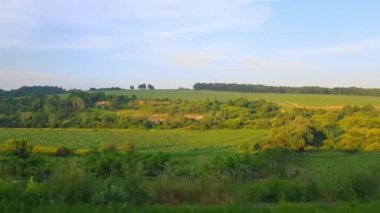 Gün batımından önce tepeler ve orman ile güzel bir manzara üzerinde yüksek hızlı tren manzarası. Arabanın penceresinden manzara, otobüs, tren. Güneşli bir günde trenden yolculuk