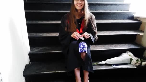 Hermosa estudiante de posgrado cintas maestras de su pierna con un yeso mientras está sentado en escaleras de metal en la universidad — Vídeo de stock