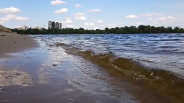 Small waves washing up a river shore with light brown sand in a sunny day. — Stock Video