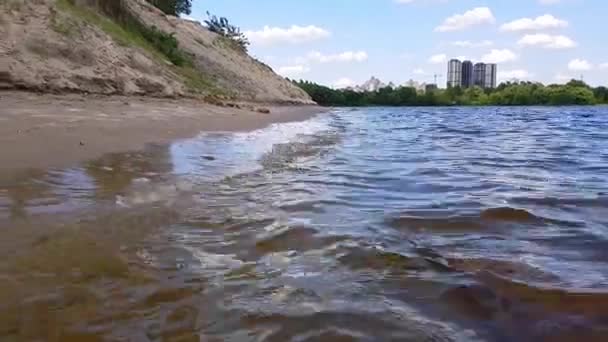 Small waves washing up a river shore with light brown sand in a sunny day. — Stock Video