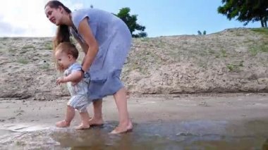 Annesiyle birlikte küçük bir çocuk kumlu kıyıya yakın suda oynuyor.
