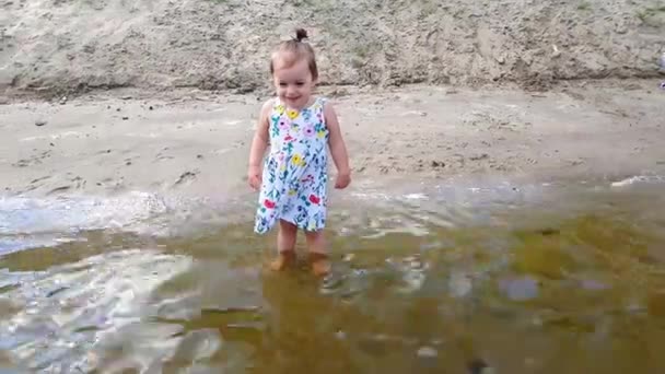 Mała dziewczynka stoi w wodzie w pobliżu brzegu w ukwiecony strój i jest szczęśliwy — Wideo stockowe